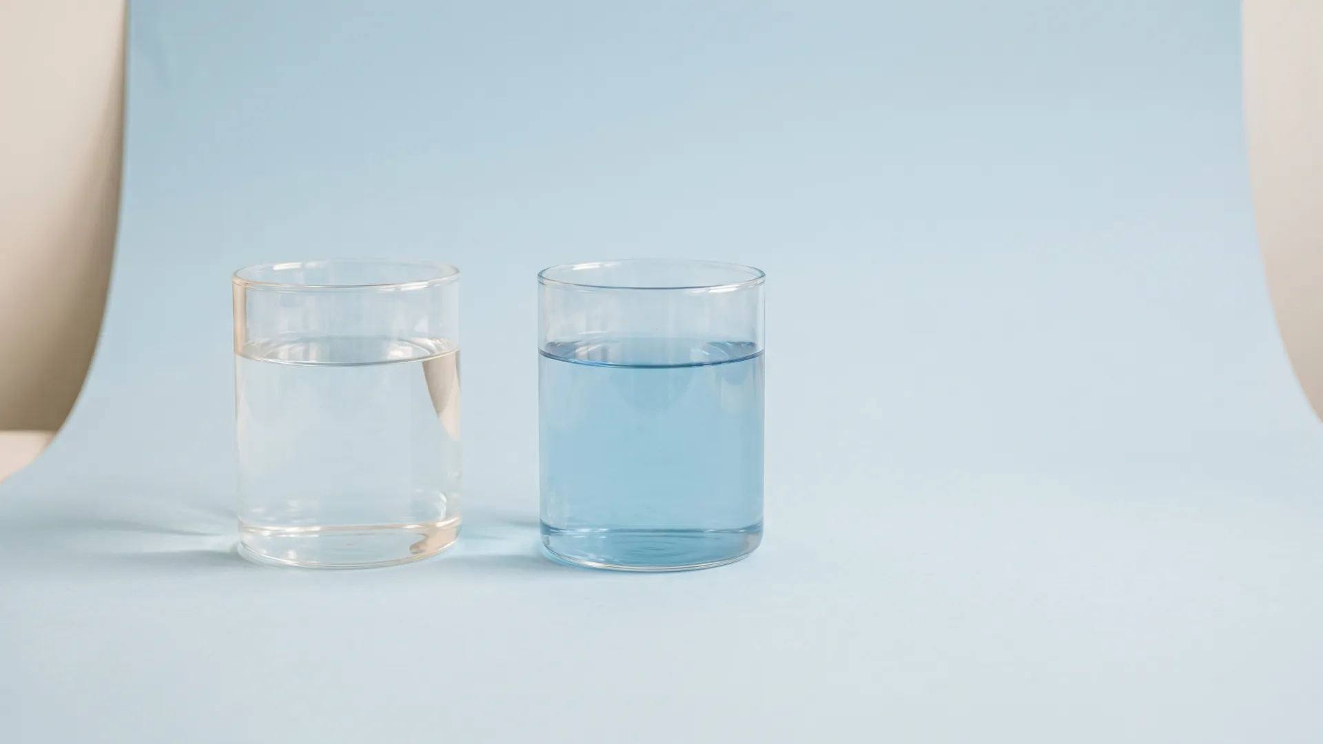 Two identical glasses side by side, one with clear water and one with pale blue water