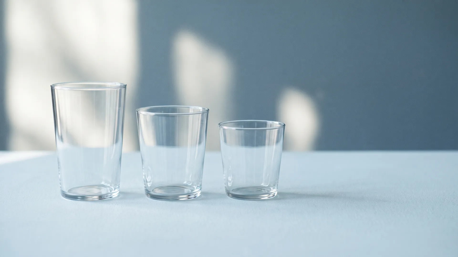 Three empty glass tumblers of decreasing size in a row on a pale blue table